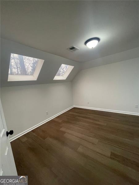 bonus room featuring dark wood-type flooring, baseboards, visible vents, and lofted ceiling with skylight