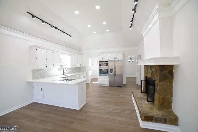 kitchen featuring light wood finished floors, a peninsula, a sink, appliances with stainless steel finishes, and backsplash