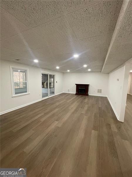 unfurnished living room with a fireplace, dark wood finished floors, visible vents, and baseboards