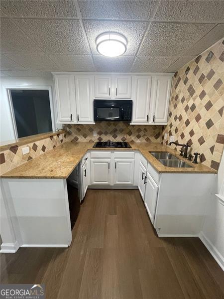 kitchen with white cabinets, dark wood-style floors, a peninsula, black appliances, and a sink