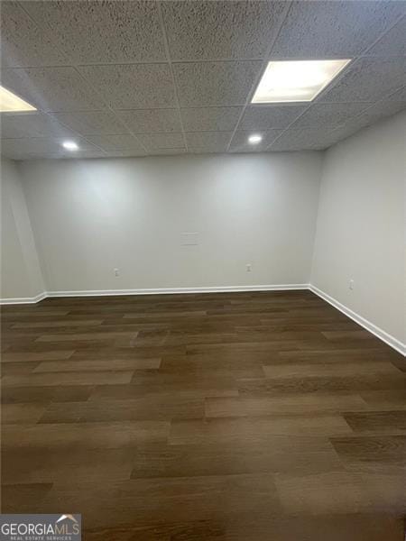 basement featuring dark wood-style floors, a drop ceiling, and baseboards