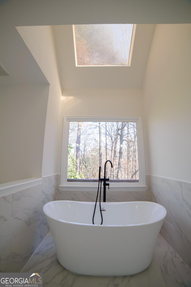 bathroom featuring a wealth of natural light, a wainscoted wall, marble finish floor, and a freestanding tub