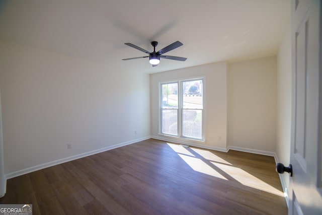 unfurnished room with dark wood-type flooring, a ceiling fan, and baseboards