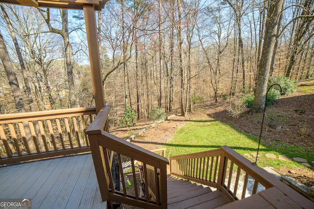wooden terrace featuring a lawn and a forest view