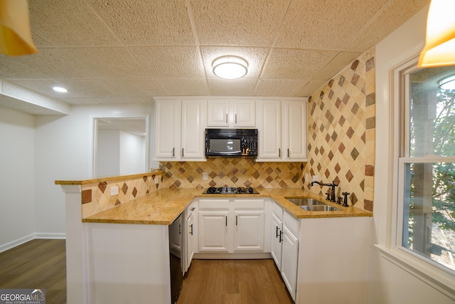 kitchen with light stone counters, a peninsula, gas stovetop, a sink, and black microwave