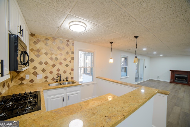 kitchen with a sink, black appliances, a fireplace, and white cabinetry