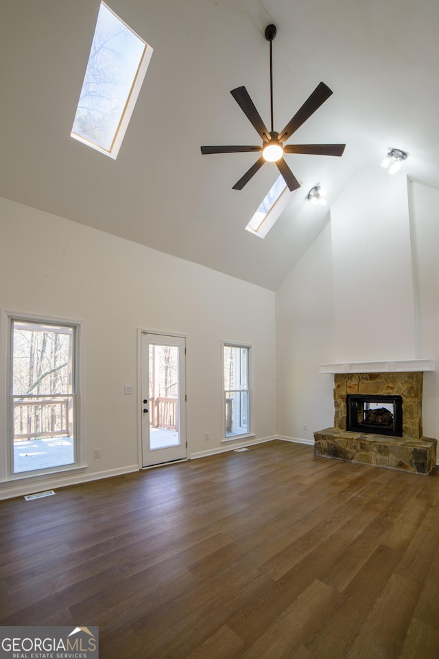 unfurnished living room with visible vents, high vaulted ceiling, a skylight, a stone fireplace, and dark wood-type flooring