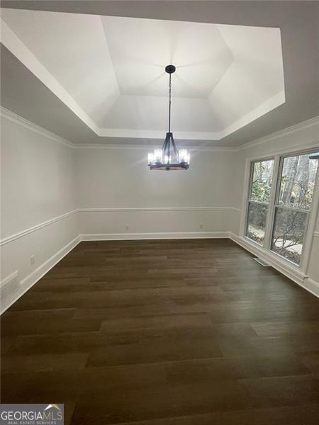 unfurnished dining area featuring dark wood-style floors, a tray ceiling, crown molding, and an inviting chandelier