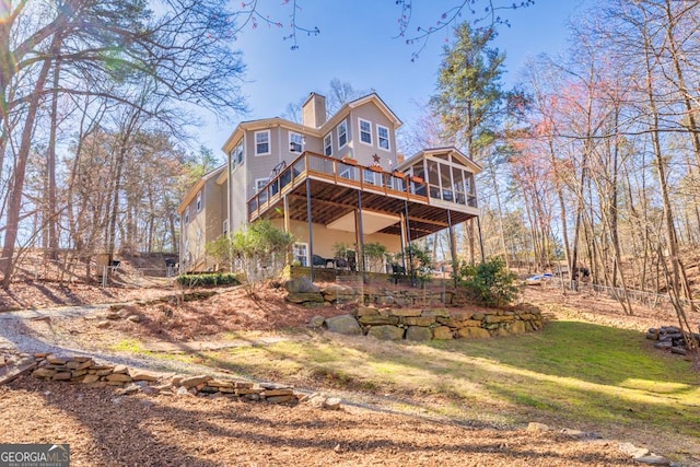 back of property with a sunroom, a chimney, a lawn, and a wooden deck