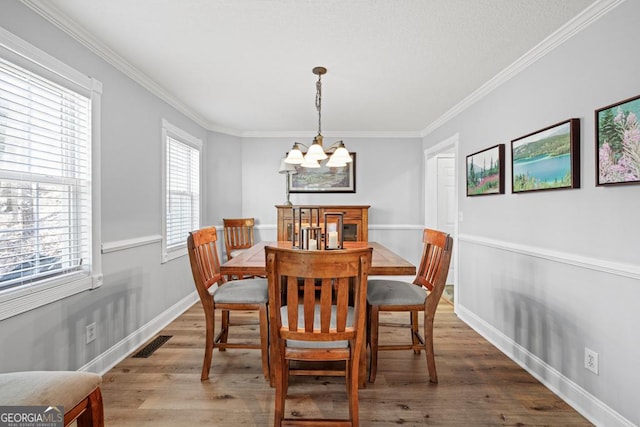 dining room with wood finished floors, visible vents, baseboards, ornamental molding, and an inviting chandelier