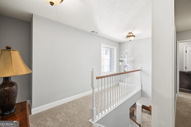 corridor with carpet floors, visible vents, a textured ceiling, and an upstairs landing