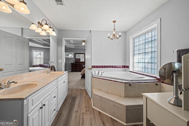 full bath with double vanity, visible vents, wood finished floors, a sink, and a bath