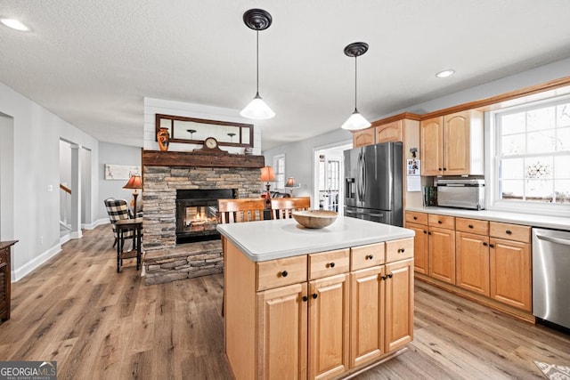 kitchen with a kitchen island, stainless steel appliances, light countertops, light wood-type flooring, and a fireplace