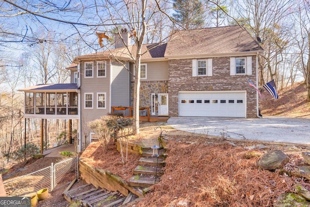 view of front of house featuring aphalt driveway, a chimney, an attached garage, a sunroom, and a gate