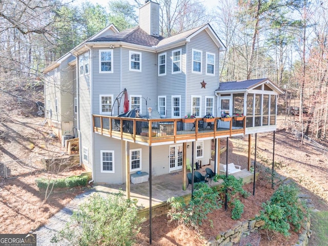 rear view of house featuring a wooden deck, a patio, a sunroom, a chimney, and french doors