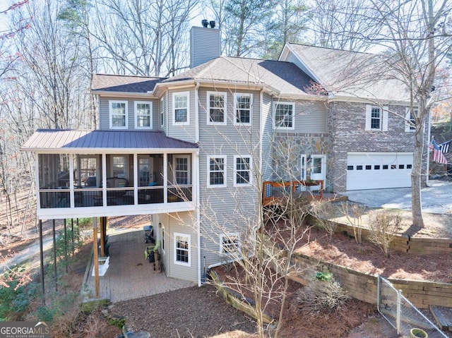 rear view of property with a garage, a sunroom, driveway, a chimney, and a patio area