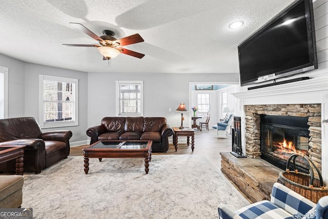 living area with a stone fireplace, plenty of natural light, and wood finished floors