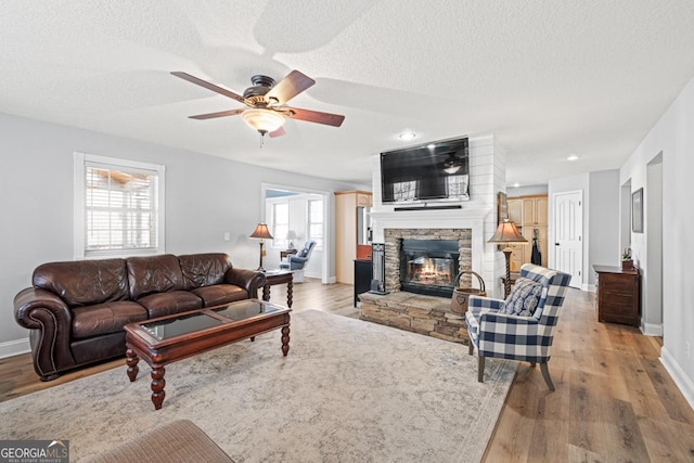 living area with light wood finished floors, a textured ceiling, and a stone fireplace