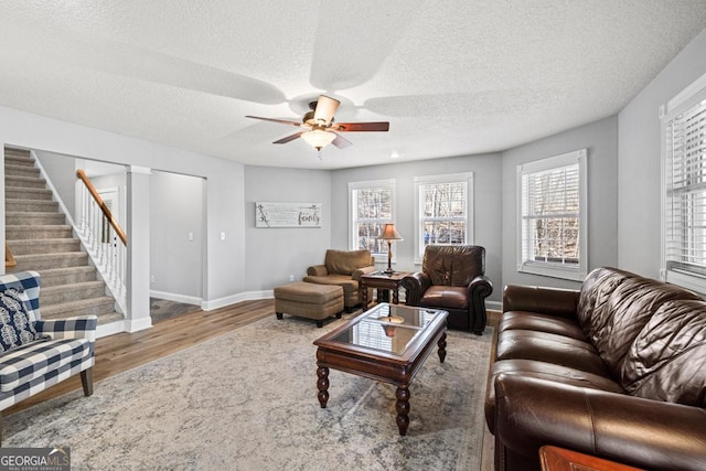 living area with ceiling fan, stairway, baseboards, and wood finished floors