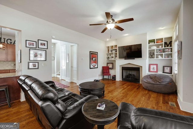 living area featuring ceiling fan, a fireplace, wood finished floors, visible vents, and baseboards