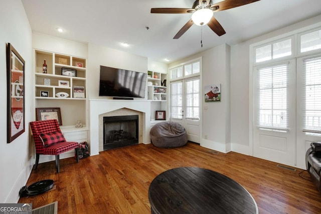 sitting room featuring built in shelves, visible vents, a fireplace, and wood finished floors