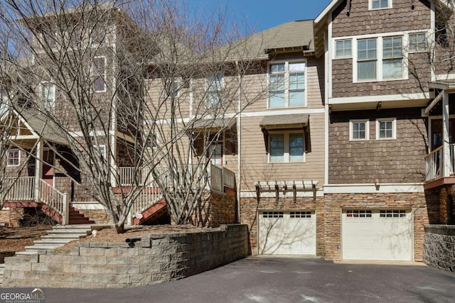 townhome / multi-family property with aphalt driveway, stone siding, a garage, and stairs