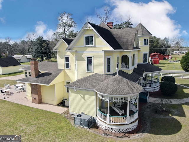 back of house featuring roof with shingles, central AC unit, a lawn, and a chimney