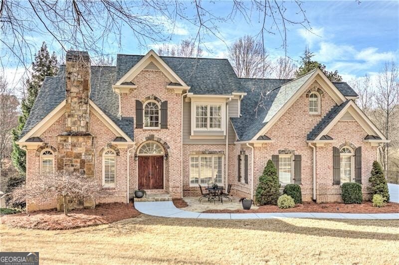 view of front of house featuring brick siding, a chimney, roof with shingles, and a front yard