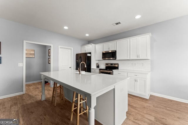 kitchen with stainless steel appliances, tasteful backsplash, visible vents, a kitchen island with sink, and a sink