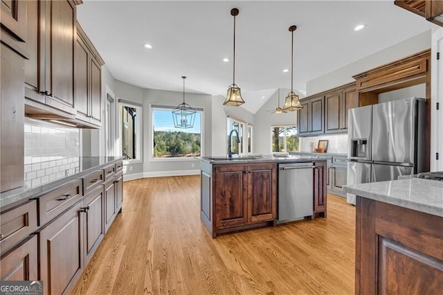 kitchen featuring stainless steel appliances, backsplash, light wood-style flooring, a kitchen island with sink, and a sink