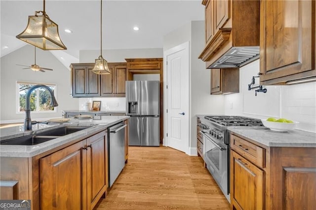 kitchen featuring light wood-style flooring, stainless steel appliances, a sink, hanging light fixtures, and custom range hood