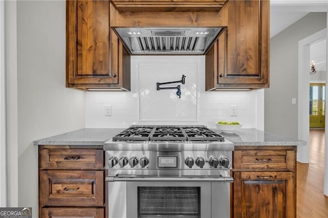 kitchen featuring light stone counters, high end stove, decorative backsplash, and ventilation hood