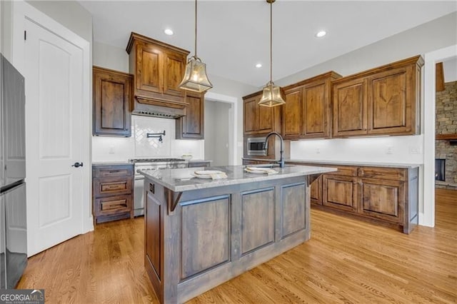 kitchen featuring a center island with sink, light countertops, light wood-style flooring, appliances with stainless steel finishes, and a sink