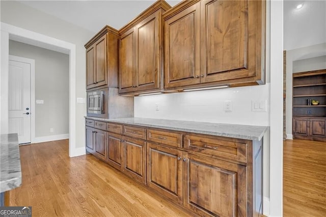 kitchen featuring light wood-type flooring, light stone countertops, baseboards, and brown cabinets