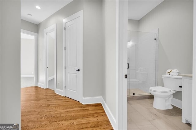 full bathroom with toilet, a stall shower, baseboards, and wood finished floors