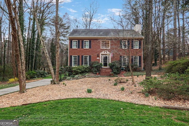 colonial home featuring brick siding, a chimney, and a front yard