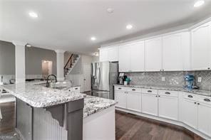 kitchen with a kitchen bar, dark wood-type flooring, backsplash, stainless steel fridge with ice dispenser, and a large island with sink