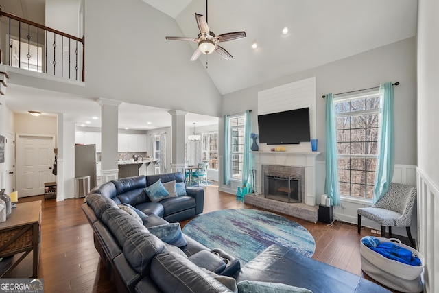 living area with a ceiling fan, wood finished floors, ornate columns, high vaulted ceiling, and a fireplace