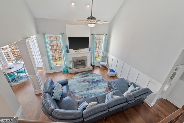 living area featuring high vaulted ceiling, a fireplace with raised hearth, wood finished floors, wainscoting, and ornate columns