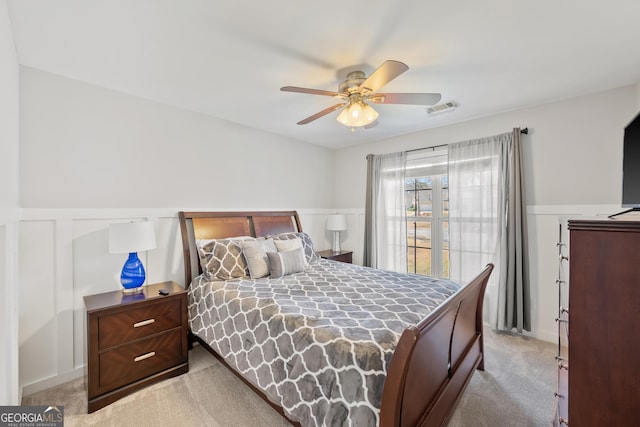 bedroom with wainscoting, a ceiling fan, visible vents, and light carpet