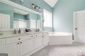 bathroom featuring lofted ceiling, a garden tub, double vanity, and a sink