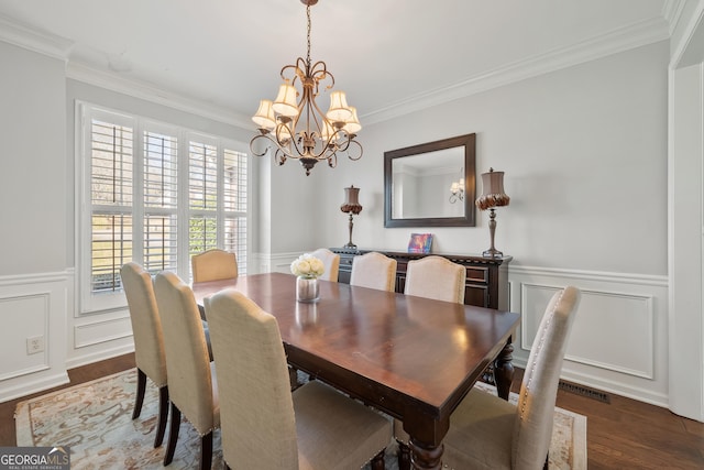 dining space featuring wainscoting, a notable chandelier, wood finished floors, and crown molding