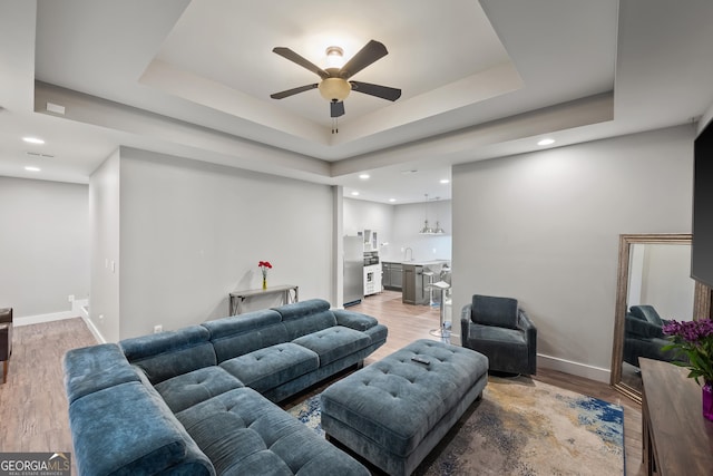 living area featuring a tray ceiling, baseboards, light wood-type flooring, and ceiling fan