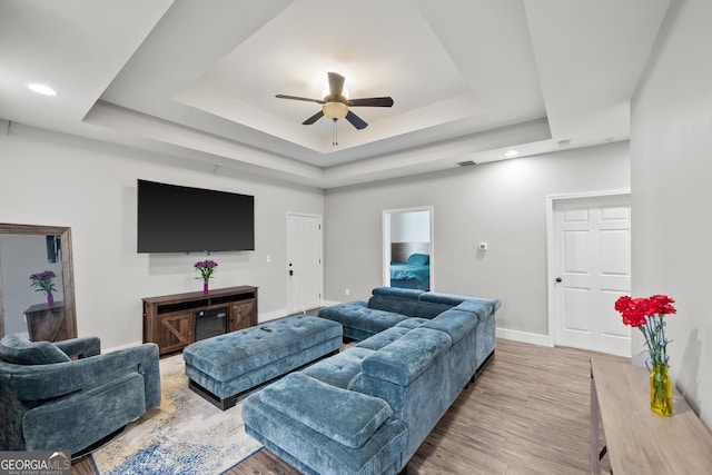 living area with baseboards, light wood-style floors, a tray ceiling, and a ceiling fan