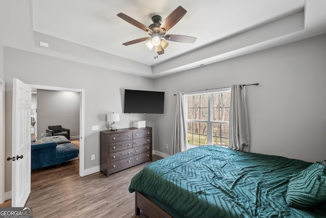 bedroom featuring ceiling fan, a tray ceiling, baseboards, and wood finished floors