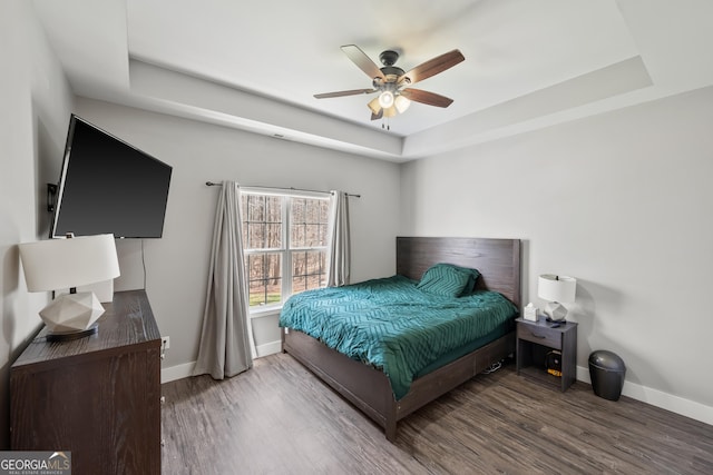 bedroom with baseboards, a tray ceiling, and wood finished floors