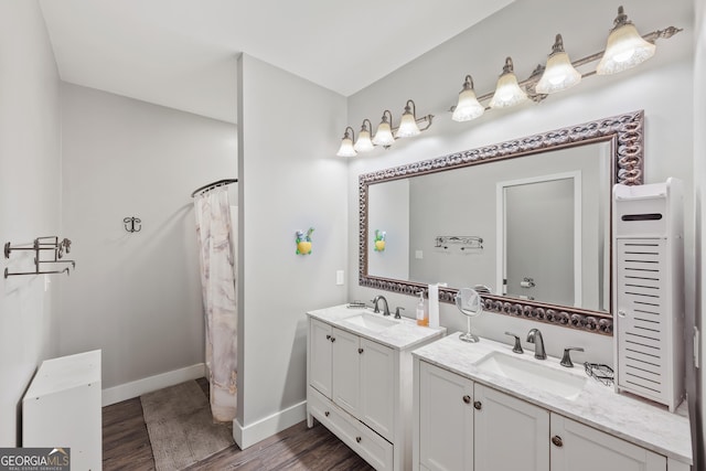 bathroom featuring wood finished floors, two vanities, baseboards, and a sink