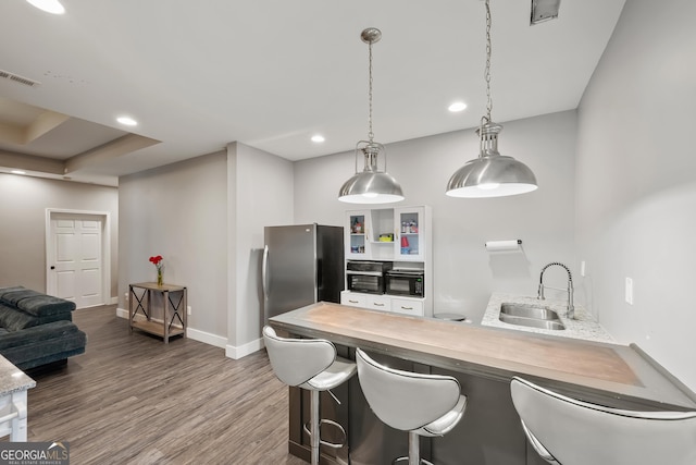 kitchen featuring visible vents, a peninsula, dark wood-style flooring, freestanding refrigerator, and a sink