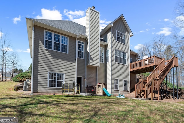 rear view of house with a deck, a trampoline, a yard, stairway, and a chimney