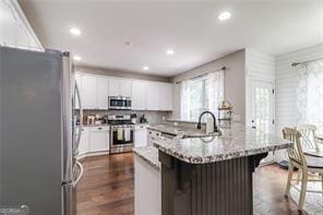 kitchen with dark wood-type flooring, a breakfast bar area, light stone counters, white cabinets, and stainless steel appliances